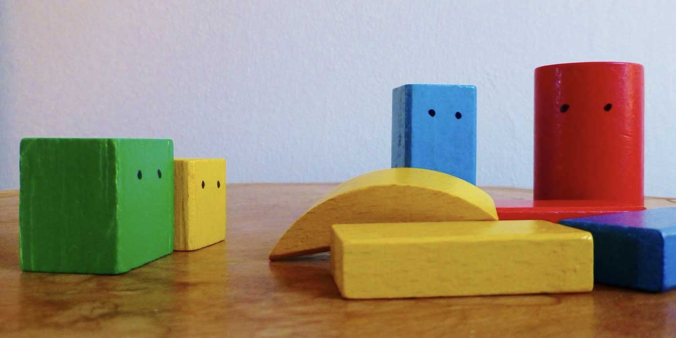 Bunte Bausteine mit Gesichtern stehen und liegen auf einem Tisch herum.
